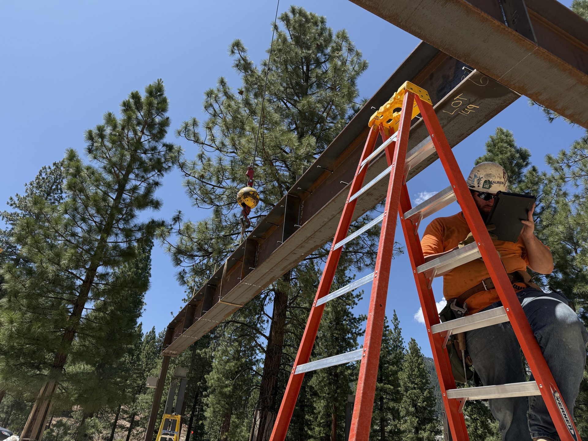 Battle Born welder on ladder reviewing drawings on iPad under steel beam